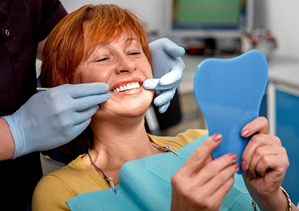 A senior woman admiring her new dentures in a hand mirror