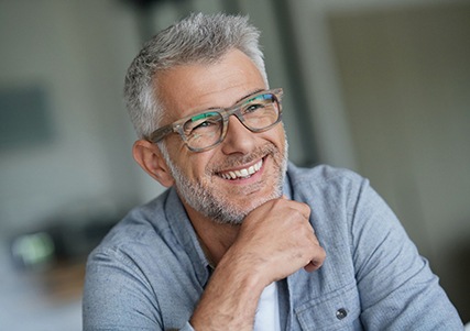 Man with greying hair and glasses smiling with dentures