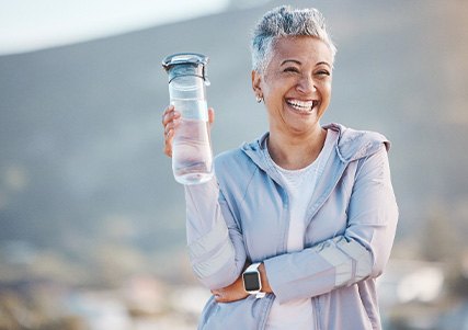 Woman smiling with water bottle on hike outside