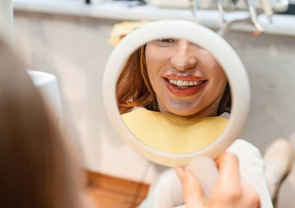 Patient with clear aligners smiling at reflection in mirror