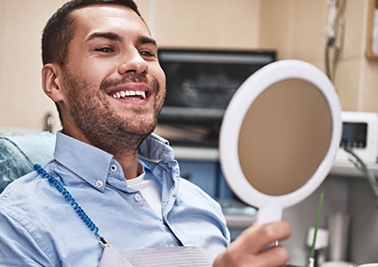 Man smiling in the dental chair while looking in circular mirror