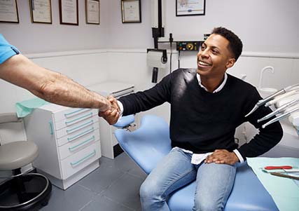 Patient and dentist shake discussing cost of dental emergencies in Saginaw