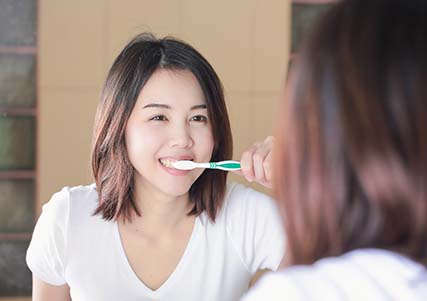 Woman brushing her teeth to prevent dental emergencies in Saginaw