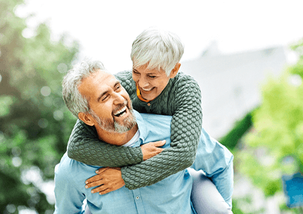 Senior man carrying senior woman on back, both laughing