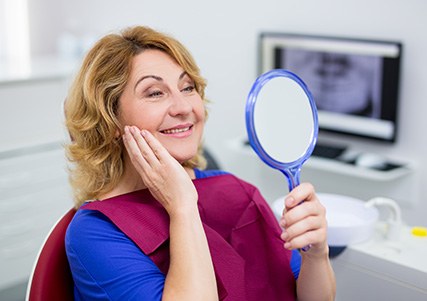 Woman in dental chair checking smile in handheld mirror