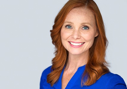 A middle-aged woman with red hair and wearing a blue blouse smiling after receiving her metal-free restoration