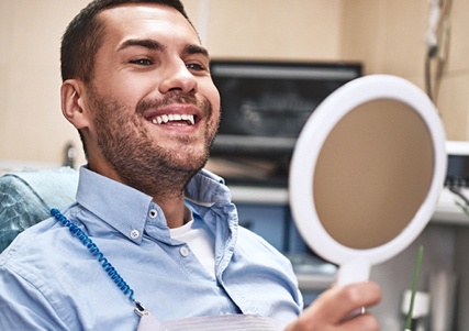 Man in blue looking at his smile in the mirror