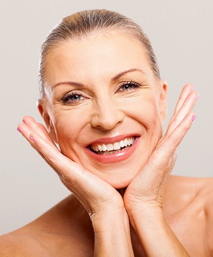 An older woman with her head between her hands and smiling after undergoing a smile makeover in Saginaw