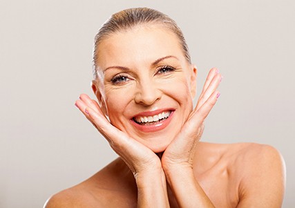 An older woman with her head between her hands and smiling after undergoing a smile makeover in Saginaw