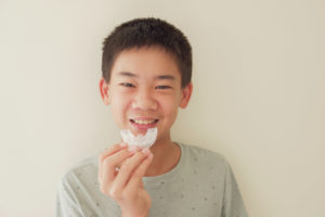 Smiling preteen boy holding clear mouthguard in Saginaw