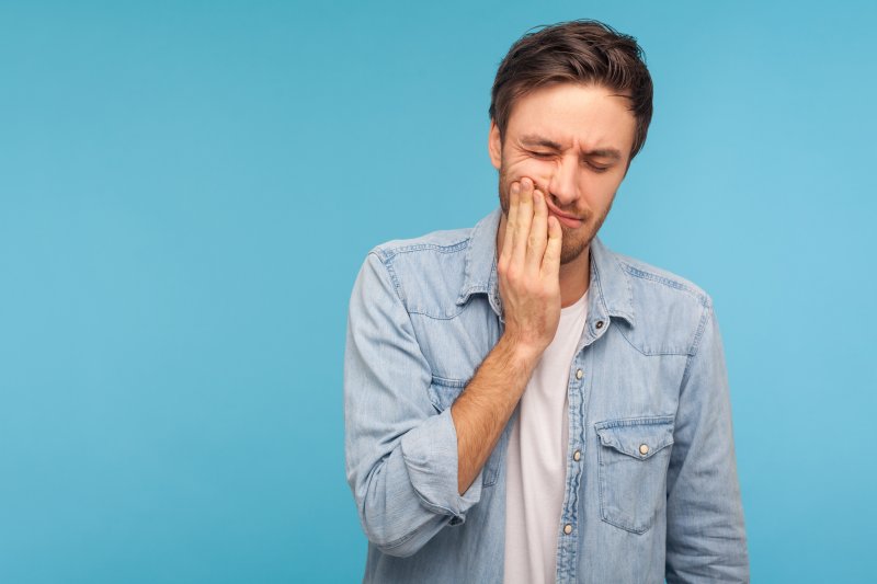 man holding cheek with ill-fitting dentures in Saginaw