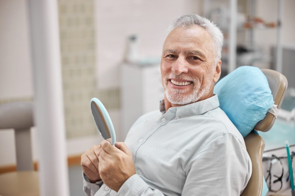 older man smiling at dentist and holding mirror