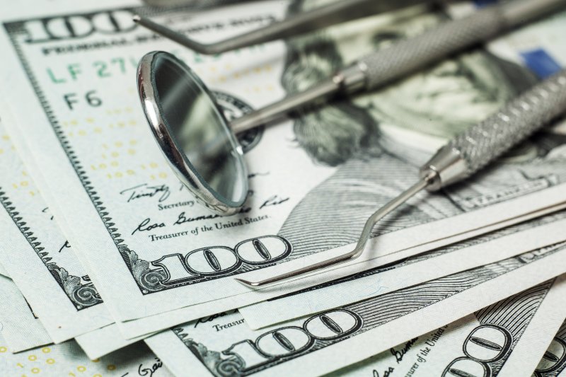 money with dental instruments lying on top